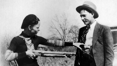 Bonnie Parker mockingly points shotgun at Clyde Barrow. American bank robbers and lovers Clyde Barrow (1909 - 1934) and Bonnie Parker (1911 -1934), popularly known as Bonnie and Clyde, circa 1933. criminal, thief, robbery team