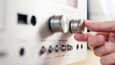 Hand turning the volume knob on a vintage stereo.