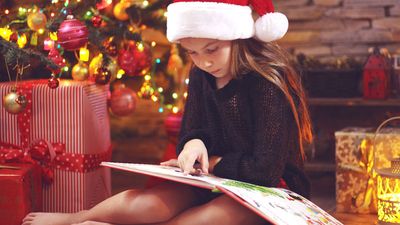 Child sitting near Christmas tree at night at home reading