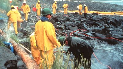 Workers pressure cleaning rocks coated in oil from the Exxon Valdez oil spill, March 1990. In the intertidal zone, Prince William Sound, Alaska. pollution disaster